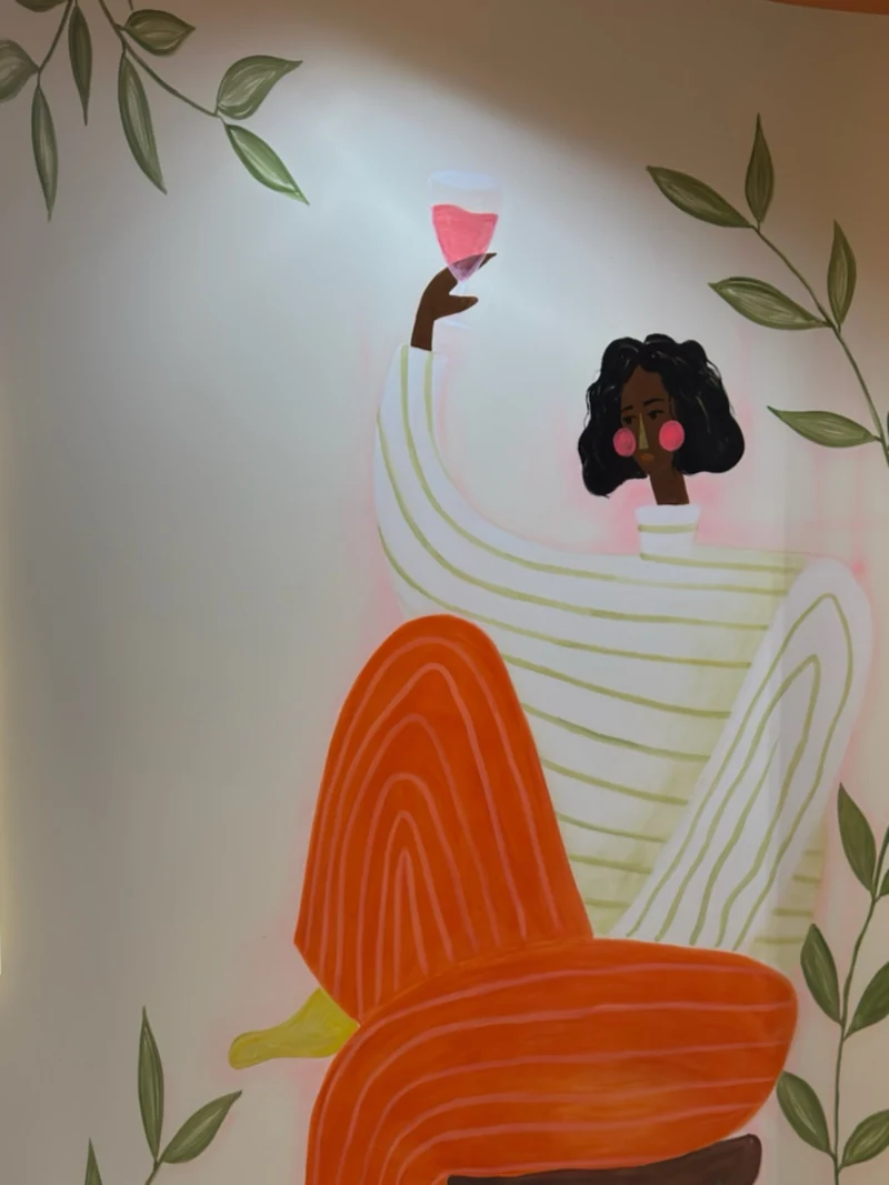 Mural žene koja drži čašu, sa narandžastim detaljima u Tries Kecu